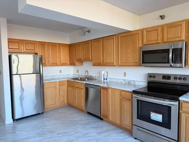 Cleaned apartment kitchen with oak cabinets, stainless appliances and marble-effect flooring